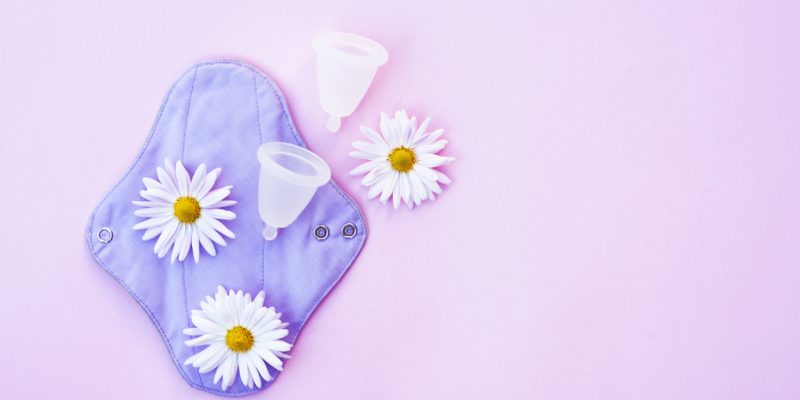 Reusable pad and menstrual cup with daisies on pink fogn. Zero waste concept. Ecological product.